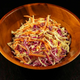 Wooden bowl filled with coleslaw on a dark background