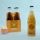 A 12oz bottle of Boylan Crème Soda with a pack of four bottles in the background, alongside a cupcake. All items are displayed against a light blue background.