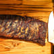 Two-thirds of a raw Dragon’s Breath #3 rib rack coated in a dark spice rub, trailing off the page with a large kitchen knife on the side