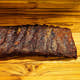 Two-thirds of a rack of Smokehouse Select ribs, sauced and sliced with the edge trailing out of frame