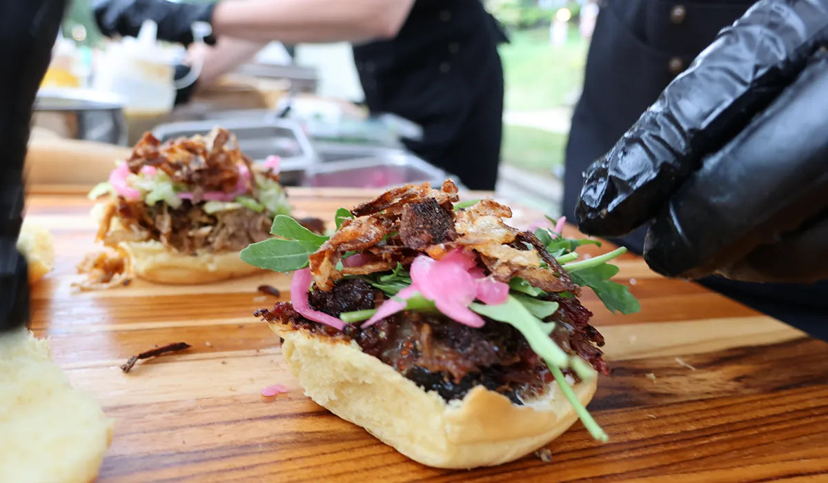Shredded beef cheek sandwich topped with arugula, pickles and crispy onions
