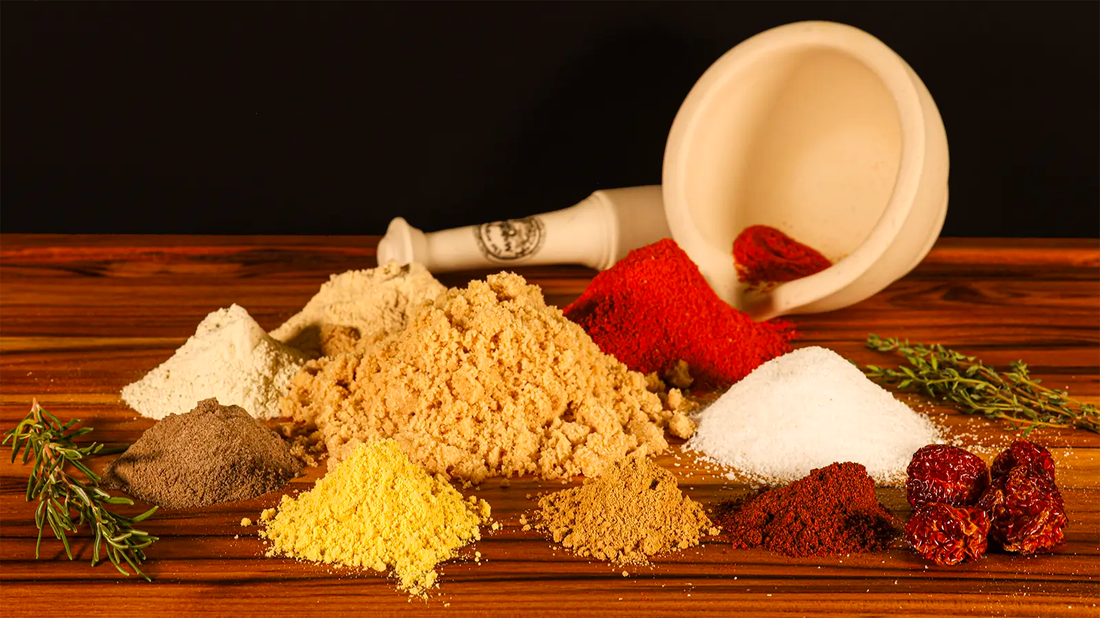 Wooden chopping board with bbq spices in small piles with a mortar in the background