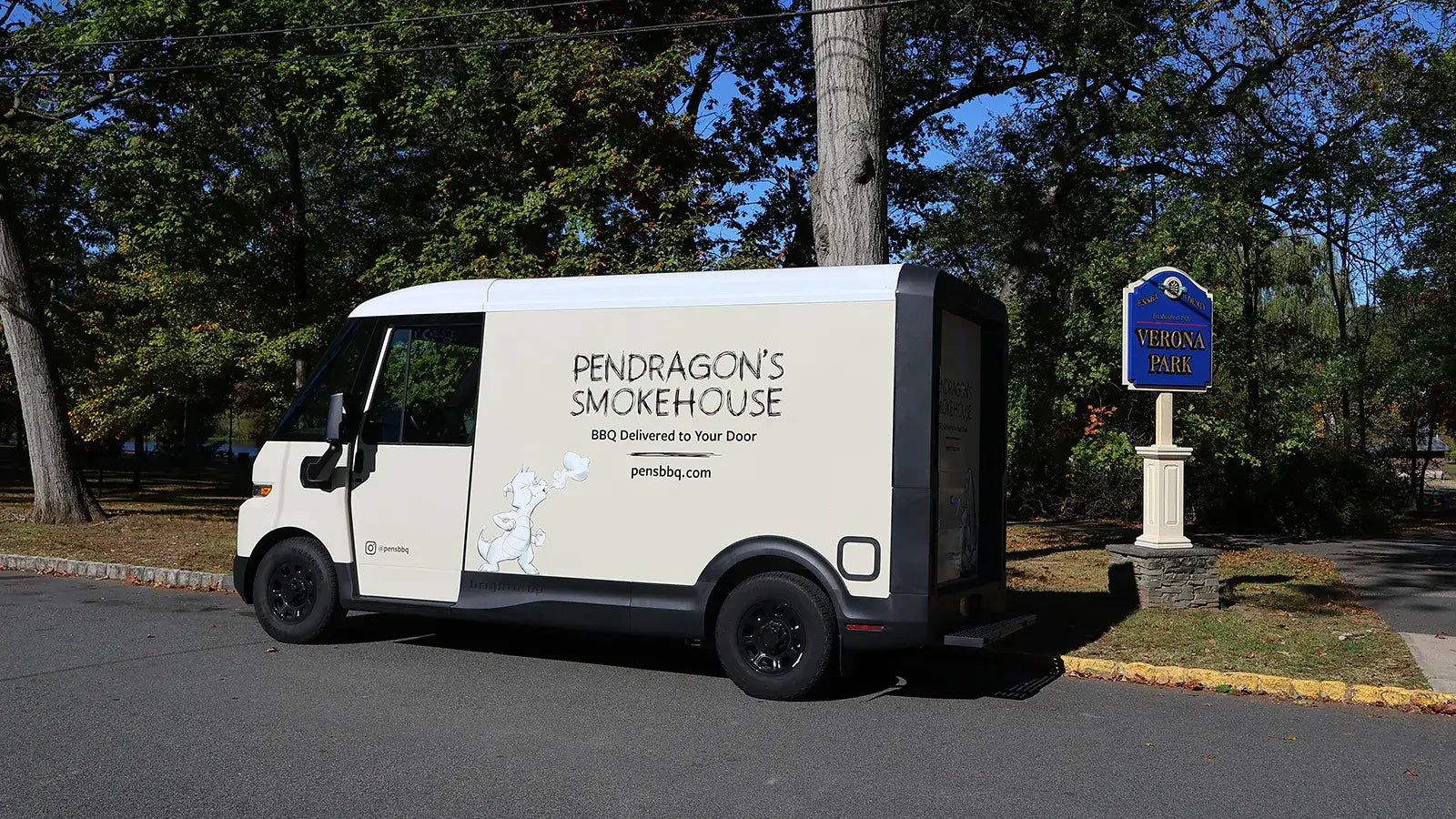 Van with 'Pendragon's Smokehouse' branding parked on a street next to Verona Park with trees and a blue sign in the background.