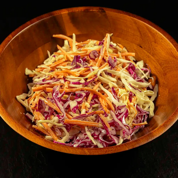 Wooden bowl filled with coleslaw on a dark background