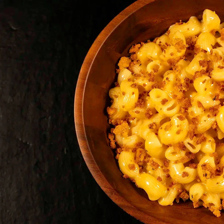 Wooden bowl of gooey macaroni and cheese on a dark background