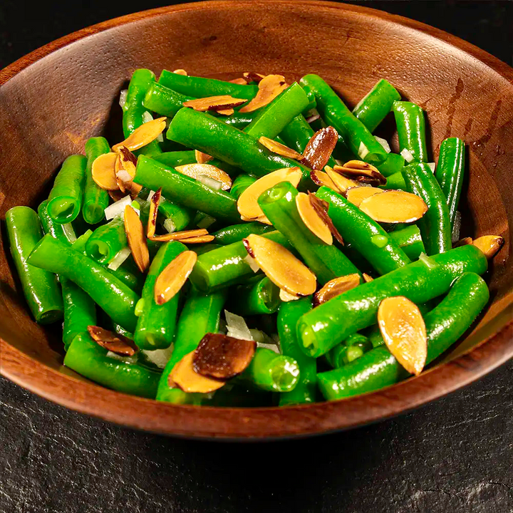 Green beans with almonds in a wooden bowl on a dark background