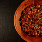 Wooden bowl filled with Pendragon's Smokehouse in house made smokey BBQ baked beans on a dark background
