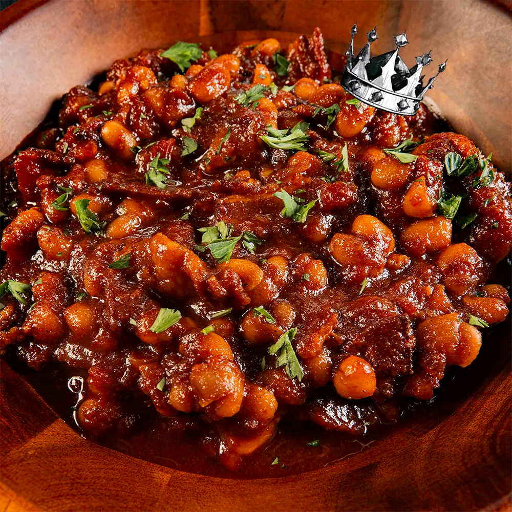 Bowl of smokey baked beans with a crown on top, in a wooden bowl