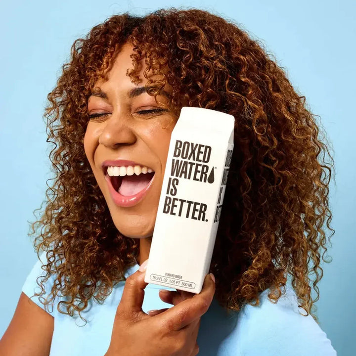 500ml boxed water from Boxed Water Is Better, offered as a sustainable drink option with Pendragon’s BBQ meals. Woman holding a bottle to her face and laughing.