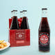 A four-pack of Boylan Cane Cola bottles next to a single bottle displayed in front, with a plate of fries in the background.