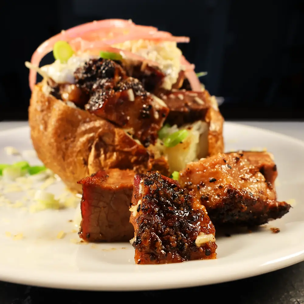 A brisket loaded baked potato with cream cheese, scallions, cheddar cheese on a white plate