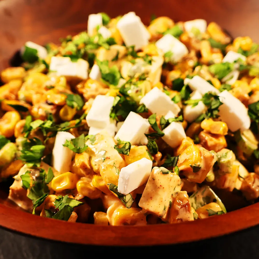 A close up of a wooden bowl showing a charred corn salad with cilantro and feta