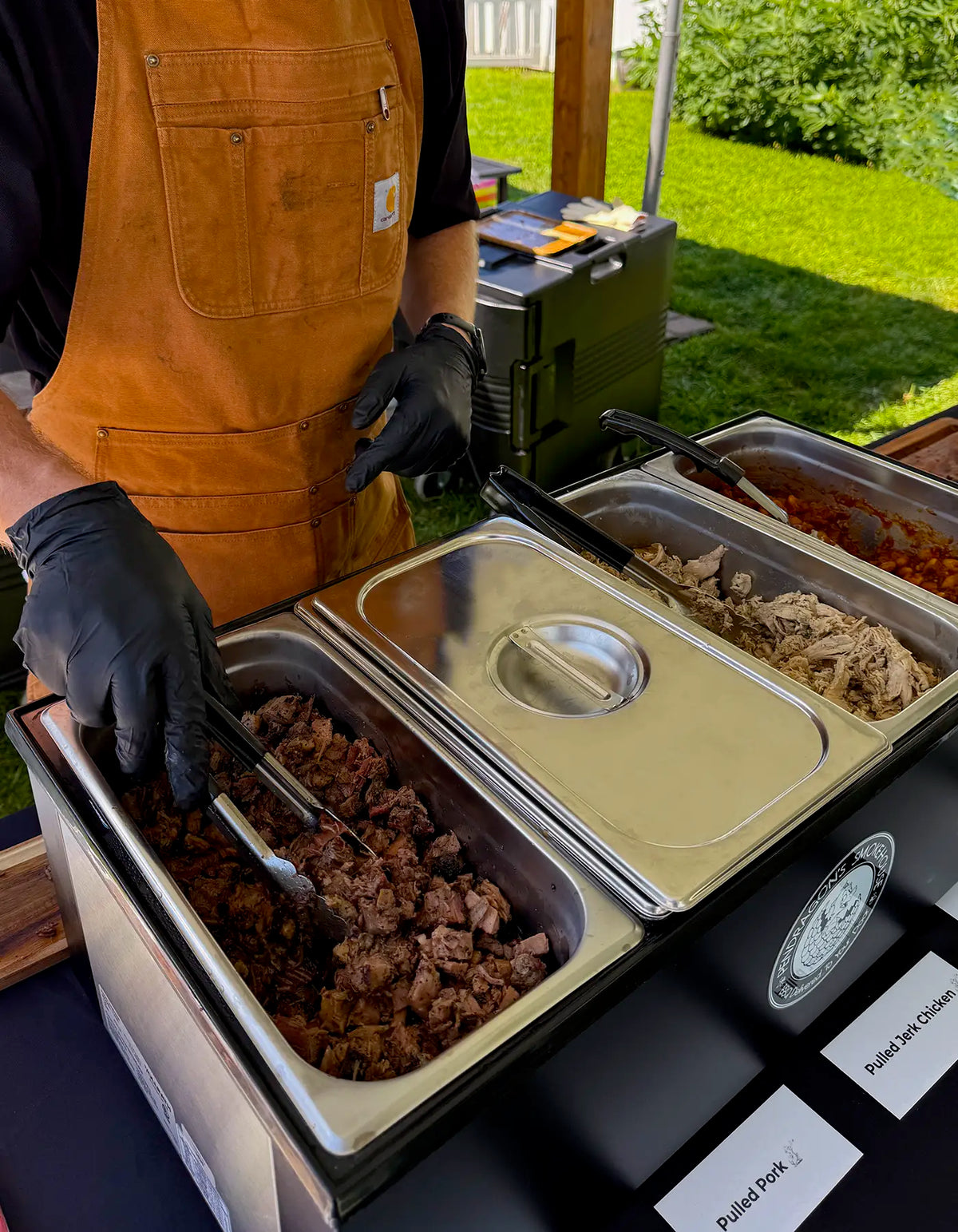 Pendragon's staff member serving brisket, pulled pork and baked beans from a baine-marie for a corporate bbq lunch