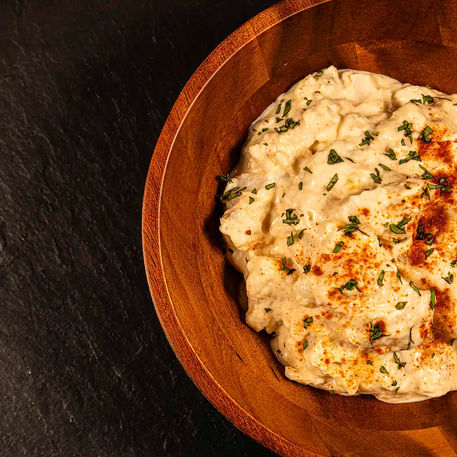 Wooden bowl with creamy potato salad garnished with herbs and paprika on a dark background