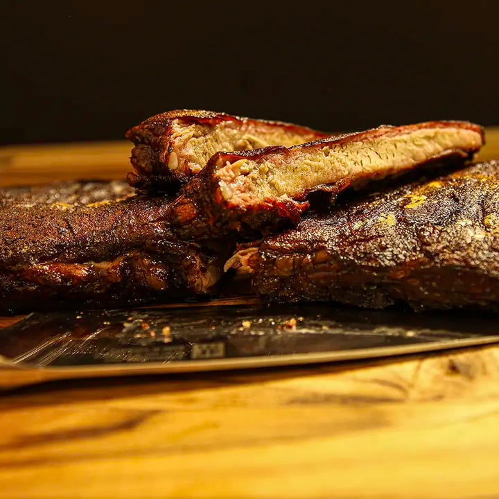 Side on image of a sliced rack of Dragon’s Breath #3 ribs with two spice-rubbed bones stacked on top, ready for delivery