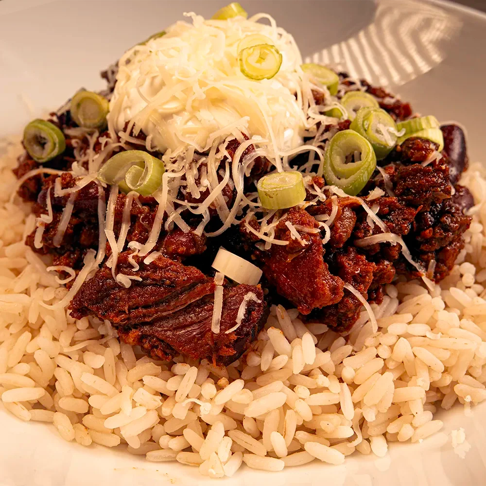 Dragon's Breath #1 Chili con carne with rice, melted cheddar, sour cream, and green onions in a white bowl