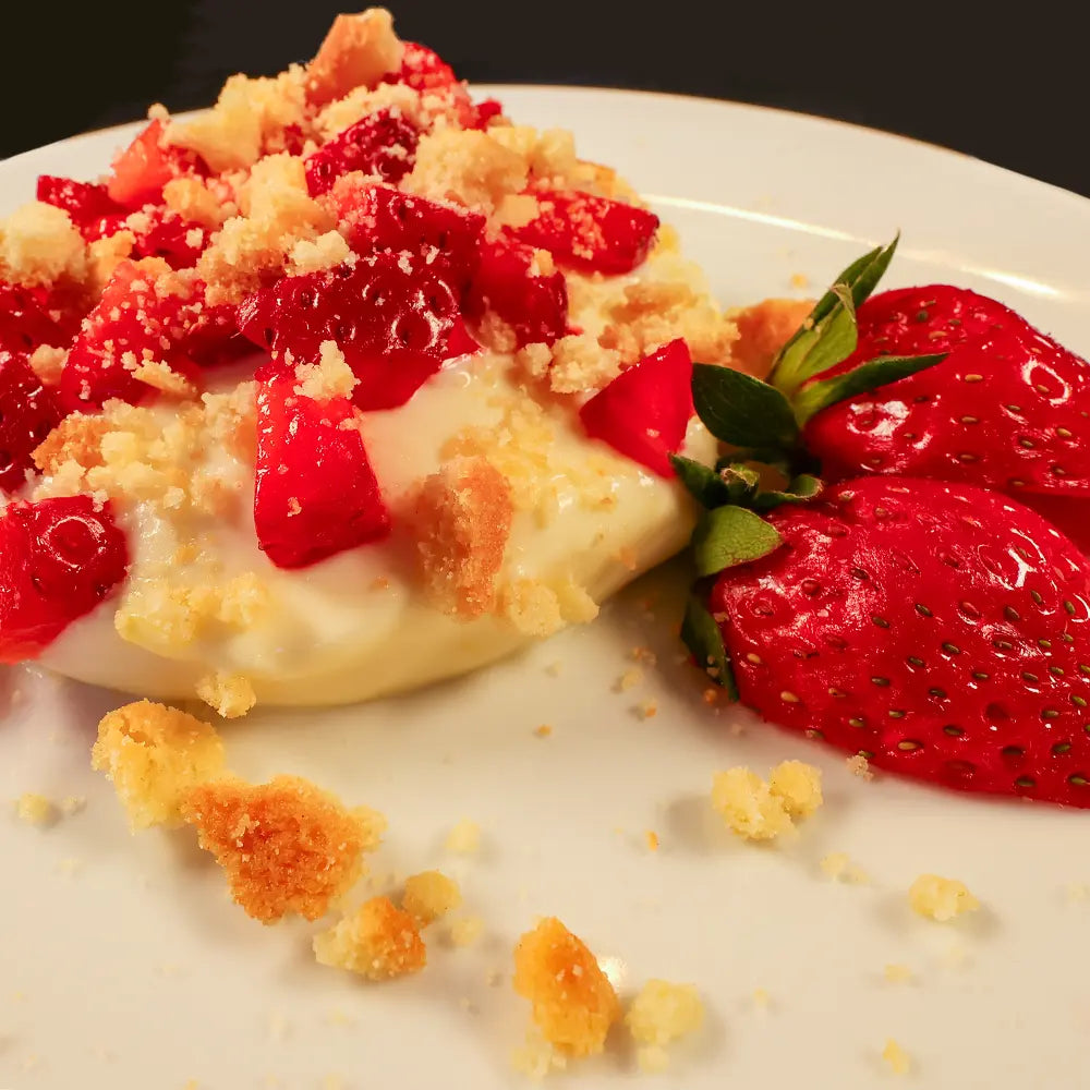 A close-up of a lemon cream pot with strawberries and shortbread crumbs ona white plate