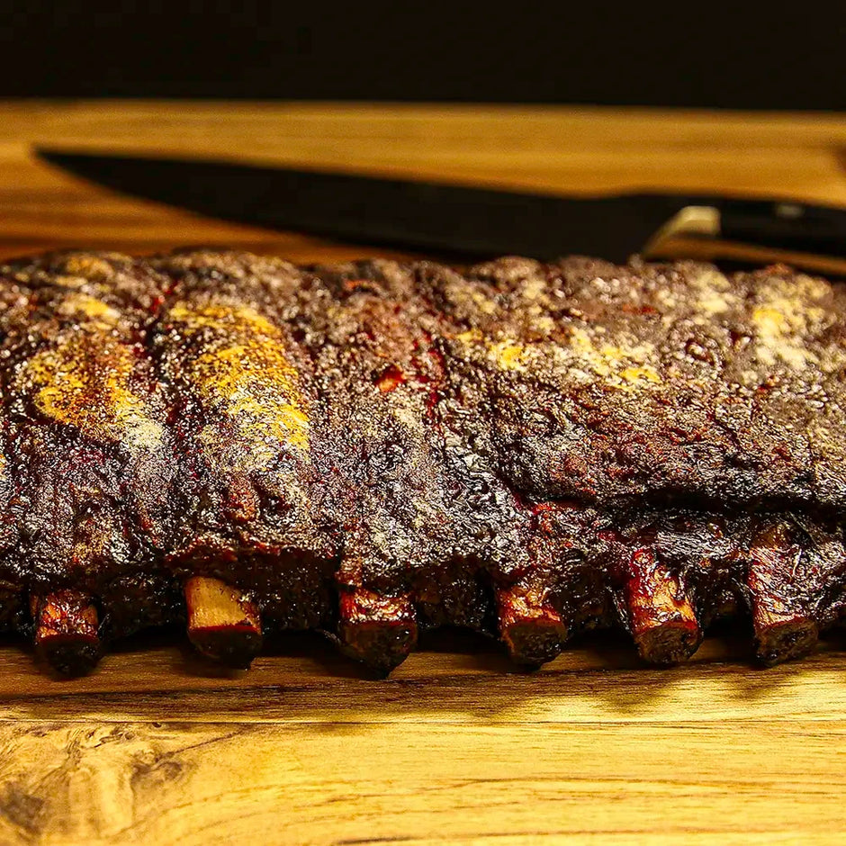 Two-thirds of a rack of Pen’s House ribs, glazed and sliced with bones disappearing out of frame and a large kitchen knife