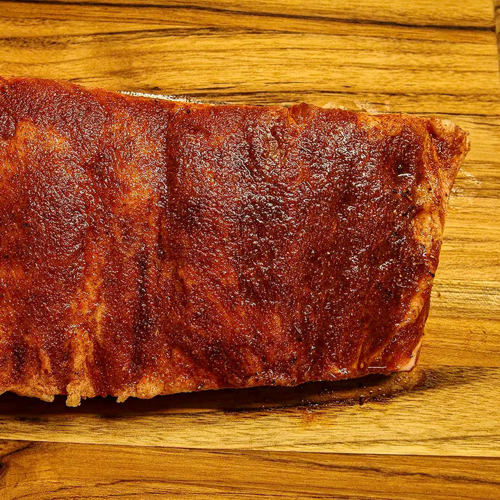 Two-thirds of a raw Pen’s House rib rack covered in dry rub, angled off-frame before cooking