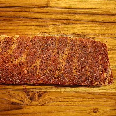 Two-thirds of a raw Smokehouse Select rib rack coated in dry rub, disappearing out of frame before smoking