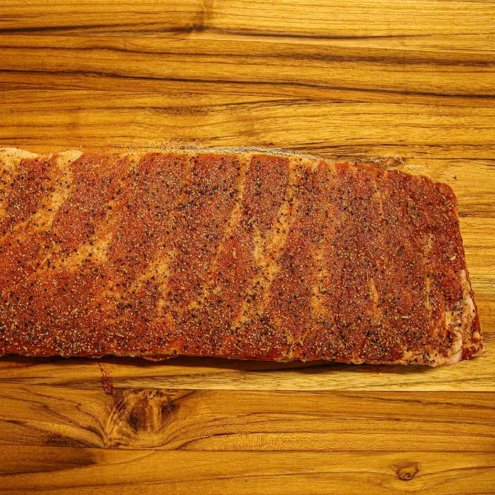 Two-thirds of a raw Smokehouse Select rib rack coated in dry rub, disappearing out of frame before smoking