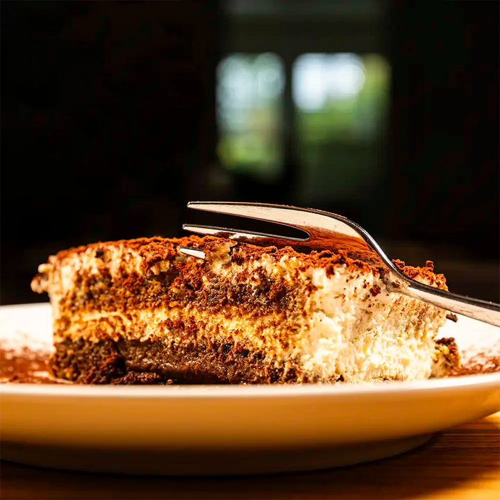 Slice of tiramisu with a fork on a white plate against a dark background