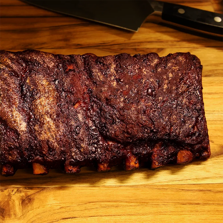 Barbecue ribs on a wooden cutting board with a knife in the background